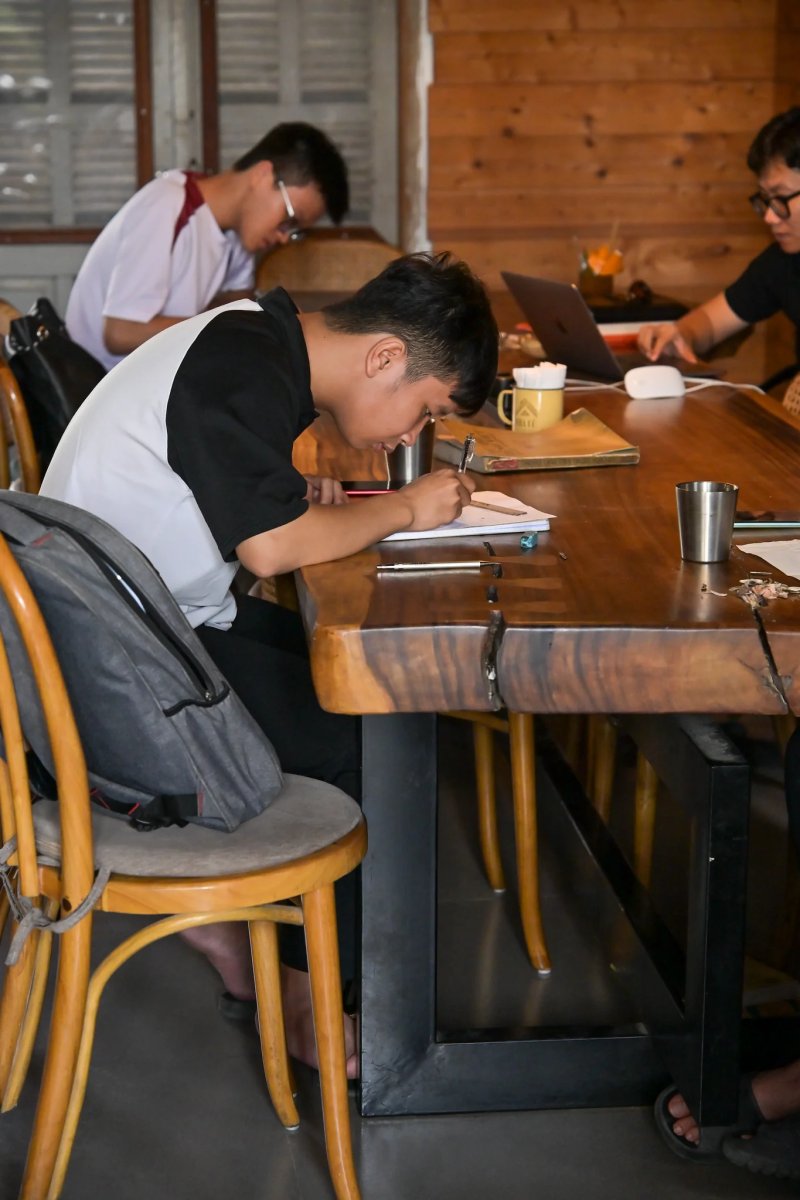 Học viên ngồi bên bàn gỗ dài, chăm chú vẽ trên trang giấy
