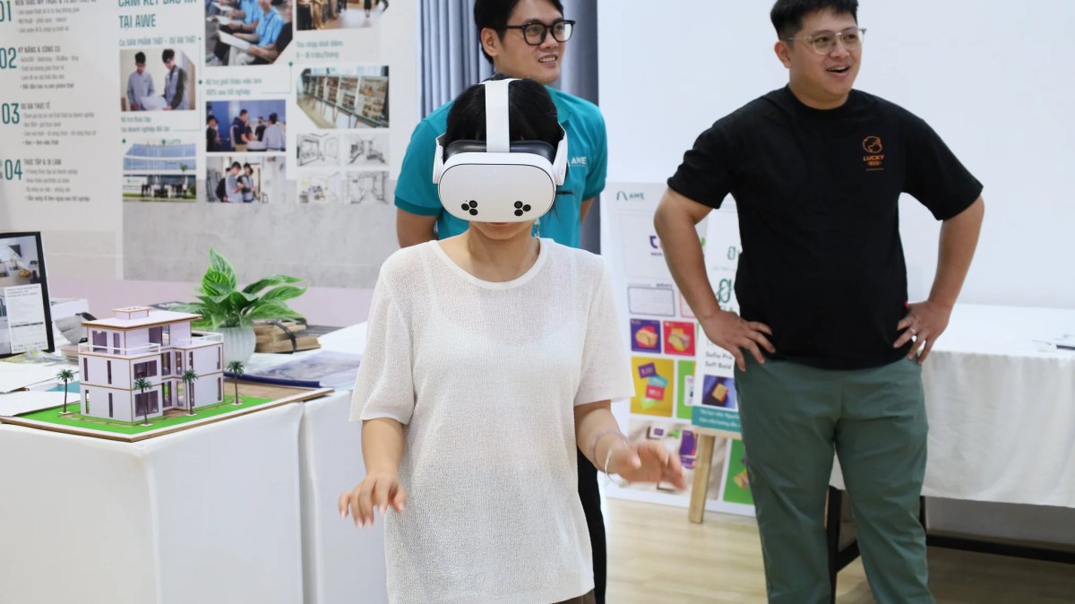 Người tham gia đeo kính VR bên bàn có mô hình nhà, hai người đứng quan sát