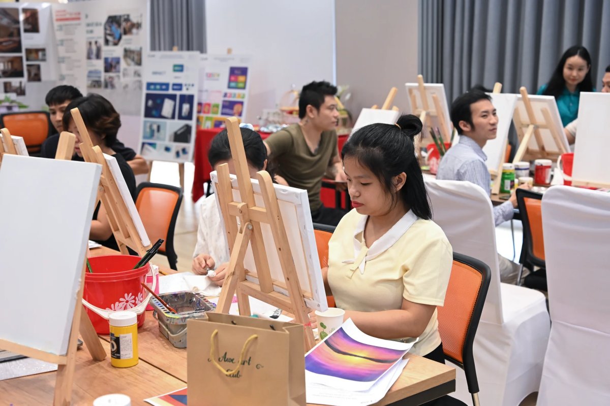 Phòng workshop với nhiều giá vẽ, mọi người đang vẽ trên toan trắng